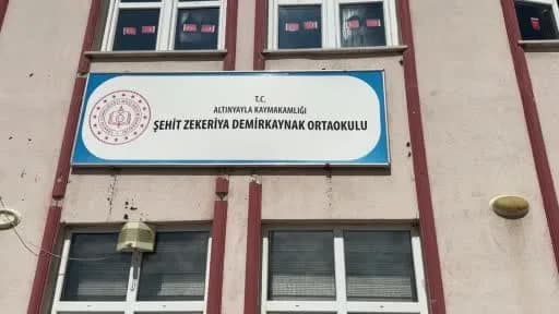 Altınyayla Şehit Zekeriya Demirkaynak Ortaokulu bahçesinde öğrenciler ve yöneticiler çevre temizliği yaparken ve duvarla