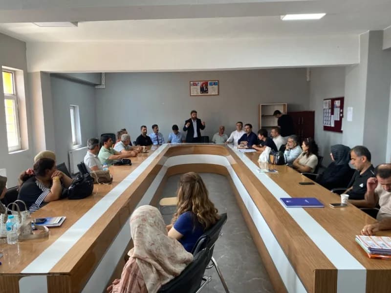 Mücahit Tekin öğretmenler odasında ayakta konuşma yapıyor, öğretmenler masada dinliyor